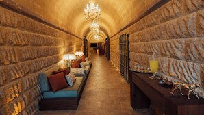A stone-walled corridor with a bench, a table with a drink, and a chandelier. - Selebrity Cappadocia (Avanos)
