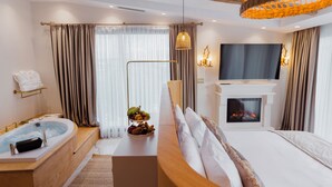 A modern hotel room with a large bed, a sitting area with a TV and fireplace, a bathtub, and a fruit bowl. - Selebrity Cappadocia (Avanos)
