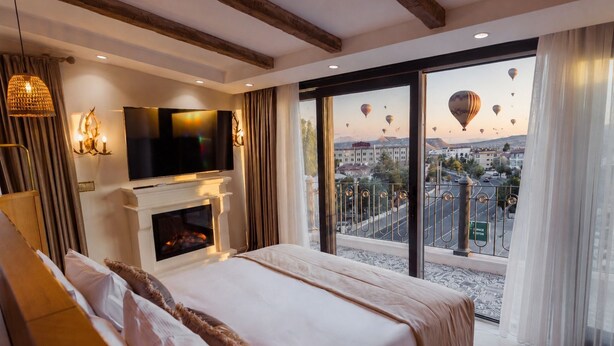 A hotel room with a large bed, a fireplace, a TV, and a balcony with a city view. - Selebrity Cappadocia (Avanos)