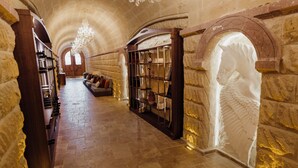 A stone-walled corridor with a chandelier, a bookshelf, and a statue. - Selebrity Cappadocia (Avanos)