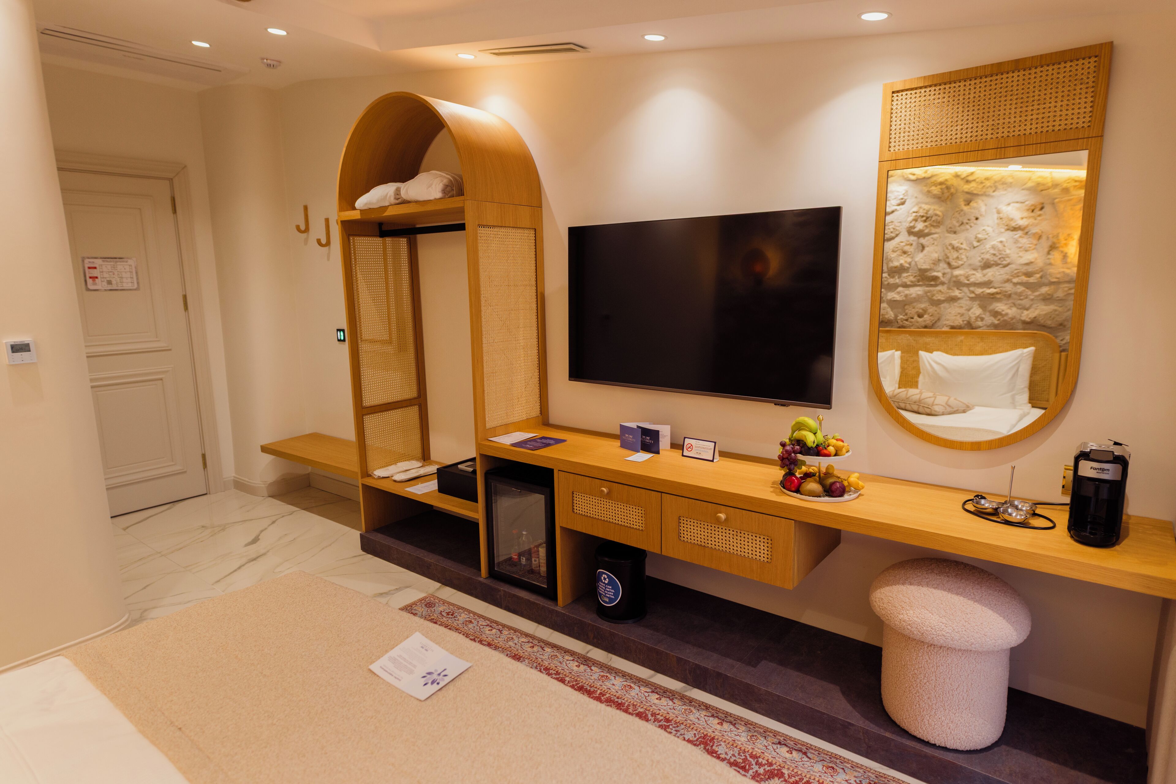 Ein Hotelzimmer mit einem Holzkonsolentisch, einem Flachbildfernseher, einer kleinen Kühlbox, einer Bank und einem großen Spiegel.