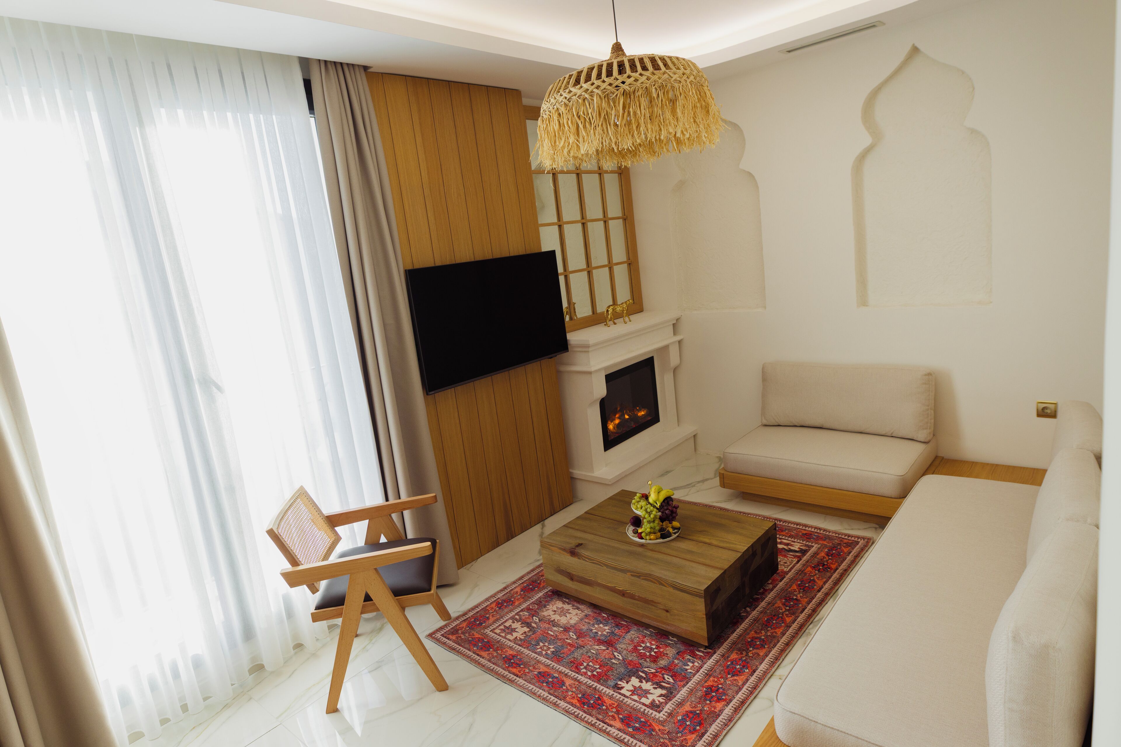 A modern living room with a sofa, a wooden coffee table, a TV mounted on the wall, a fireplace, and a patterned rug.