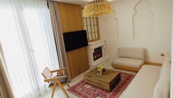 A modern living room with a sofa, a wooden coffee table, a TV mounted on the wall, a fireplace, and a patterned rug.