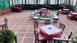 An outdoor patio with multiple tables and chairs, some covered with umbrellas. - Potter's Hill (Shimla)