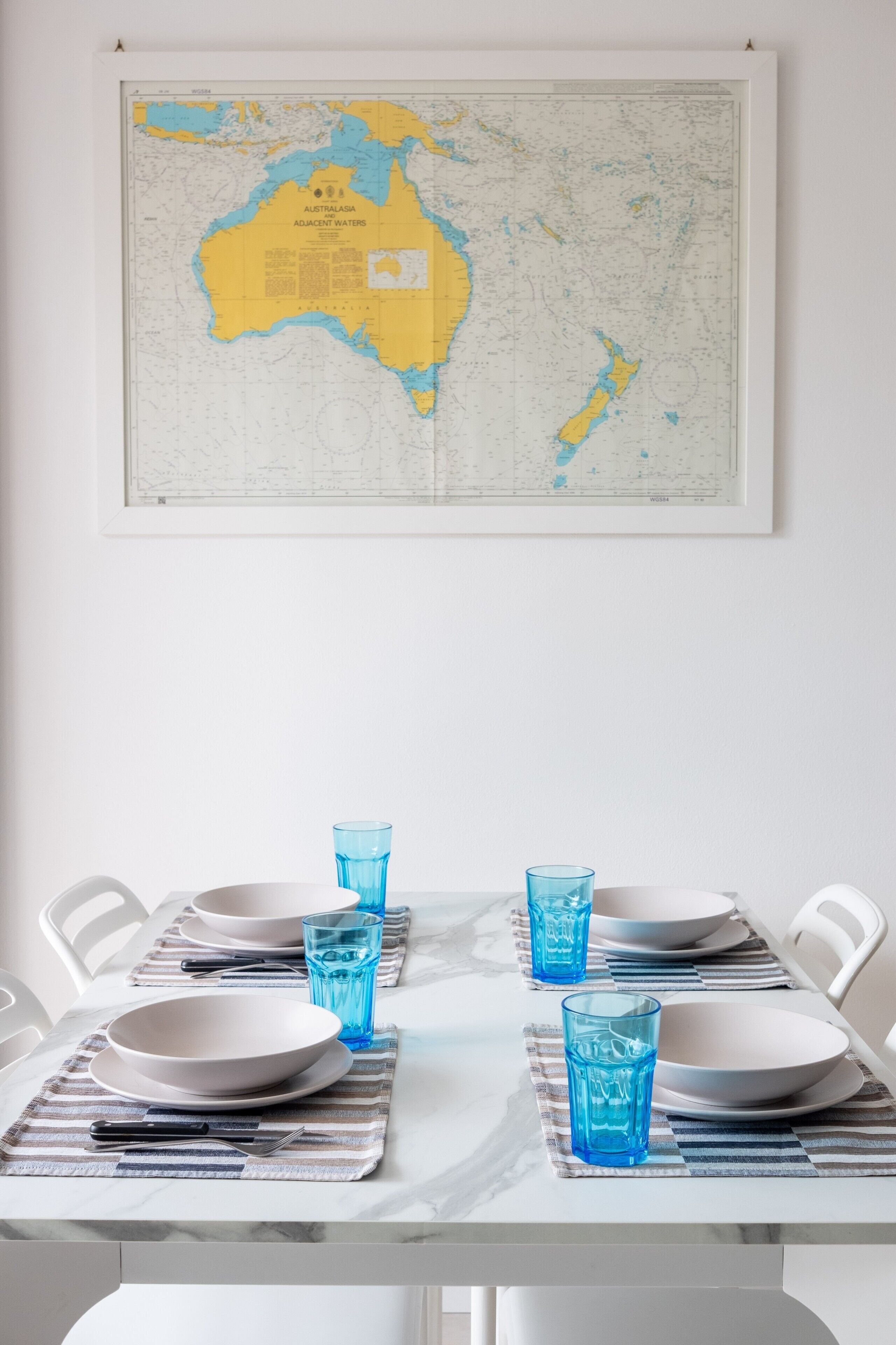 Ein Esstisch mit Tellern, Gläsern und Besteck, vor einer weißen Wand mit einer Karte darüber.
