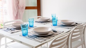 Ein Esstisch ist mit Tellern, Schüsseln und blauen Gläsern gedeckt, umgeben von weißen Stühlen.