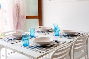 Ein Esstisch ist mit Tellern, Schüsseln und blauen Gläsern gedeckt, umgeben von weißen Stühlen.