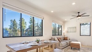 A modern living room with a wooden dining table, a sofa, and a ceiling fan. - Fraser Ridge Retreat | 3BR/3.5BA, Free WP Shuttle (Fraser)