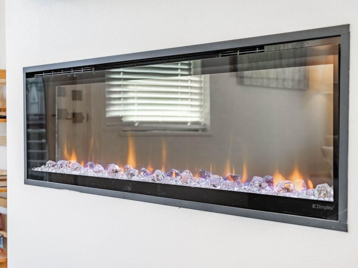 A wall-mounted fireplace with a glass front, displaying a fire burning through a bed of stones.