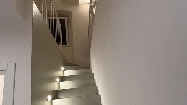 A staircase with white walls and a handrail, leading to a landing with a door and a small window. - Cozy retreat near Saturnia Hot Springs with lovely views and space for 7 guests! (Manciano)