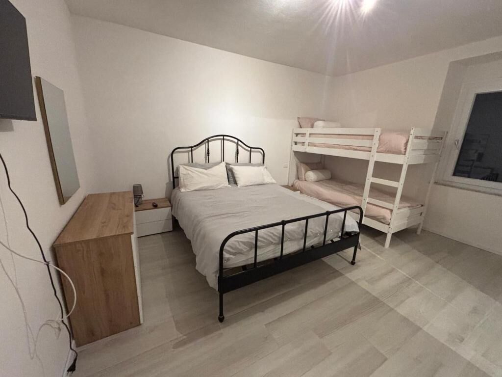 Een slaapkamer met een enkel bed, een houten nachtkastje, een witte linnenkast en een stapelbed.