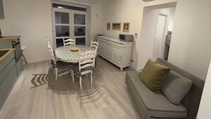 A compact living space with a dining table, chairs, a sofa, a kitchenette, and a door. - Cozy retreat near Saturnia Hot Springs with lovely views and space for 7 guests! (Manciano)