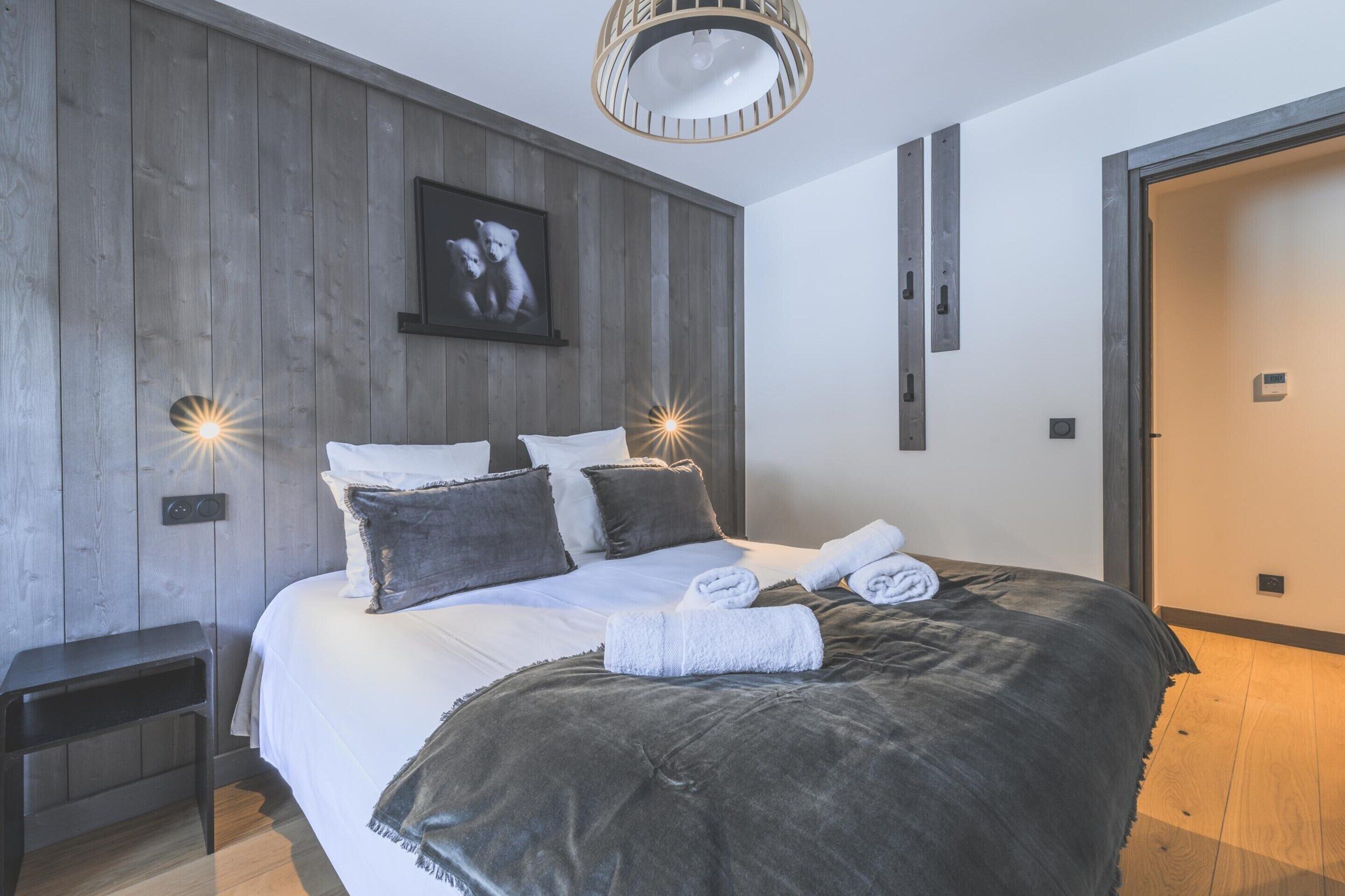 Une chambre moderne avec un grand lit, des murs recouverts de panneaux en bois, un tableau encadré et deux lampes fixées au mur.