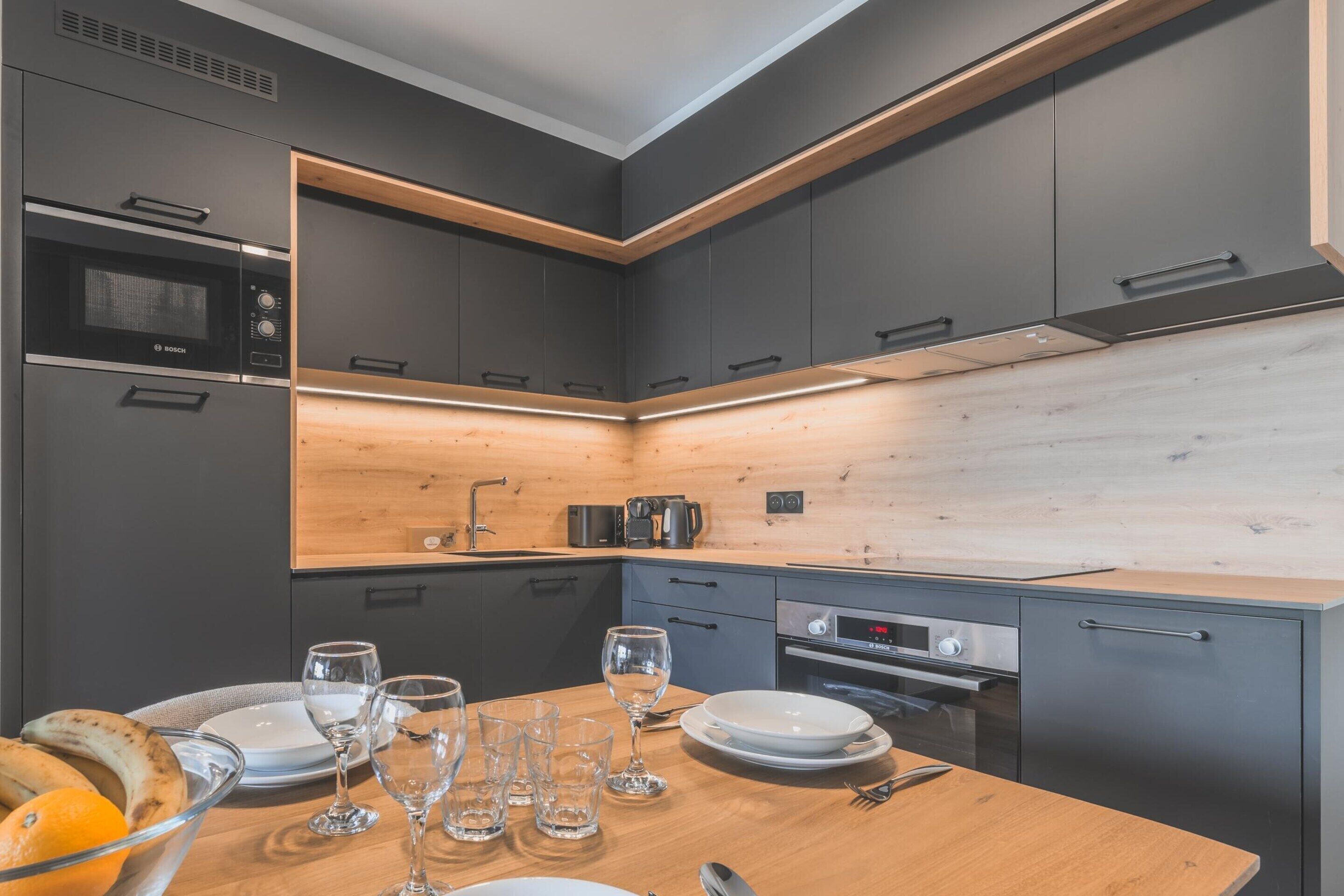 A modern kitchen with grey cabinets, a wooden countertop, and a built-in microwave.