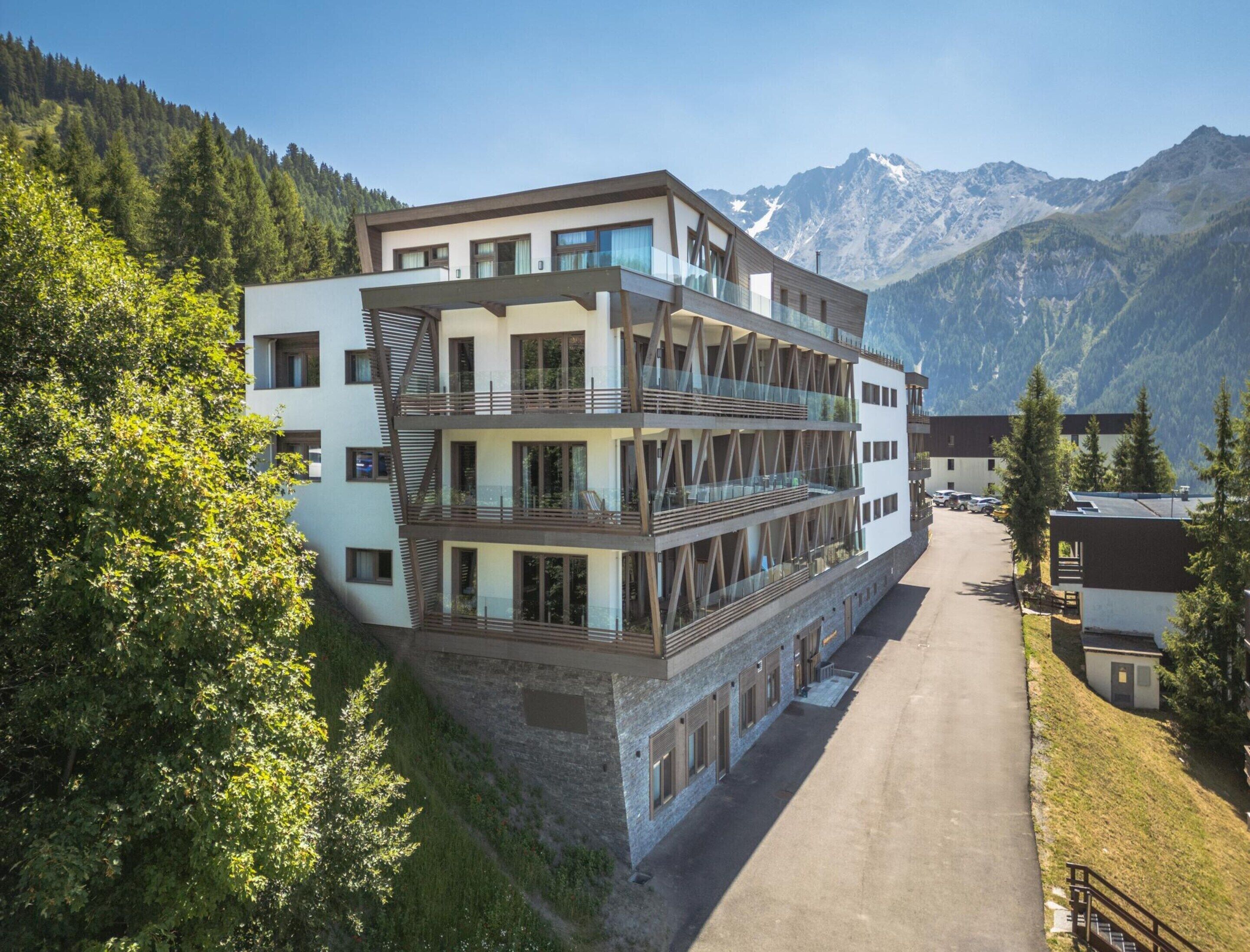 Un hotel a più piani con balconi, sullo sfondo di montagne.