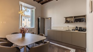 A modern kitchen with a dining area, featuring a wooden table, chairs, a built-in oven, and a microwave. - Porta Portese Palace near Trastevere (Roma)
