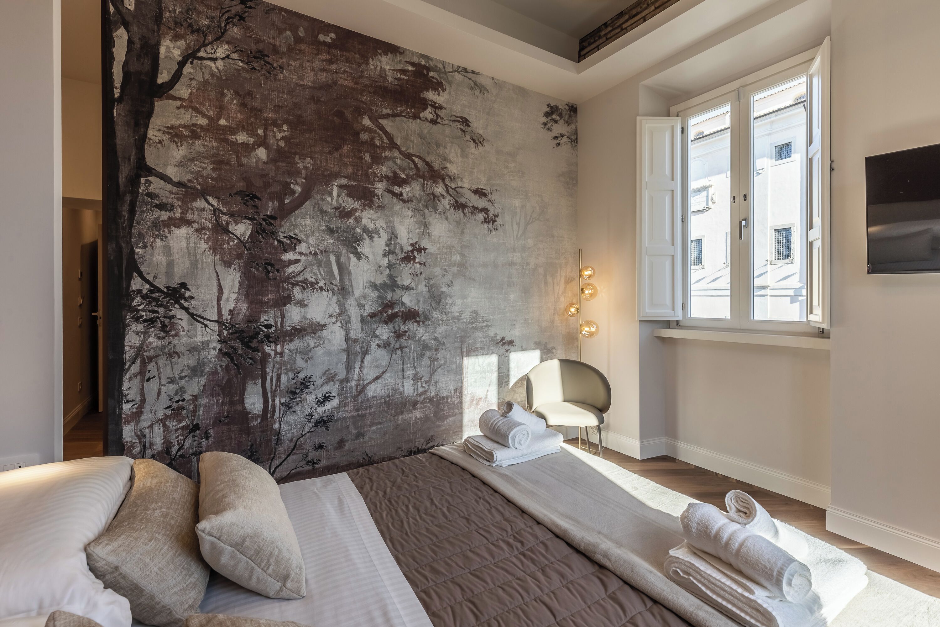 A modern hotel room with a large bed, a wall mural, a window with a view, and a chair.