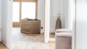 Een gang met een groot raam, een geweven mand, een hoge lamp en een roze stoel.