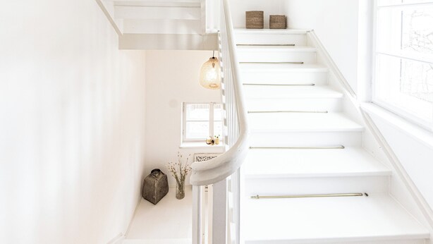 Een witte trap met een geweven lamp erboven.