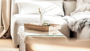 Een moderne woonkamer met een bank, een glazen salontafel en een decoratief dienblad met een kaars en een glazen vaas.