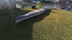 A canoe on a grassy area with a view of buildings and a body of water in the background.