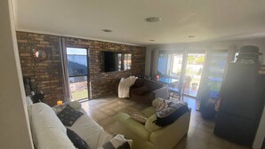 A living room with a brick wall, a flat-screen TV, a sofa, and a dining area with a table and chairs.