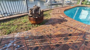A brick-paved area with a metal fence, a fire pit, and a swimming pool.
