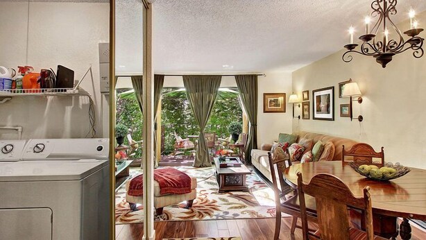 Una habitación con comedor, sofá, candelabro y vistas a través de una puerta de cristal.