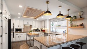 Une cuisine moderne avec des meubles blancs, des plans de travail en granit et des tabourets de bar.