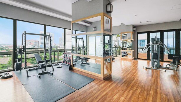 A modern gym with large windows, wooden flooring, and various exercise equipment. - Hovin by Kozystay - Tebet (Jakarta)