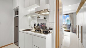 A modern kitchen with white cabinetry, a stainless steel range hood, and a window overlooking a cityscape. - Hovin by Kozystay - Tebet (Jakarta)