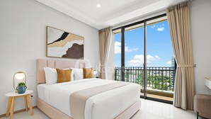 A modern hotel room with a large bed, a small side table with a lamp, a painting on the wall, and a balcony with a view of the city. - Hovin by Kozystay - Tebet (Jakarta)