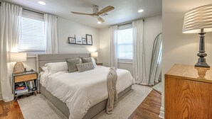 Un dormitorio con cama, mesitas de noche, ventilador de techo y una mesita con libros.