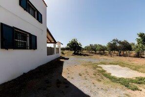 Un edificio blanco con contraventanas negras, un camino de grava y un área cercada con árboles.