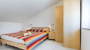 A bedroom with a bed, bedside tables, a wardrobe, and a ceiling light. - Apartment 'Spiaggia E Relax' with Private Terrace, Garden and Air Conditioning (Calasetta)