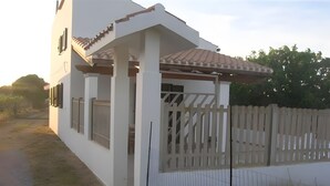 A white building with a covered porch and a white fence. - Apartment 'Spiaggia E Relax' with Private Terrace, Garden and Air Conditioning (Calasetta)