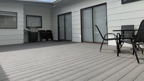 En moderne udendørs terrasse med grill, stole og et bord.