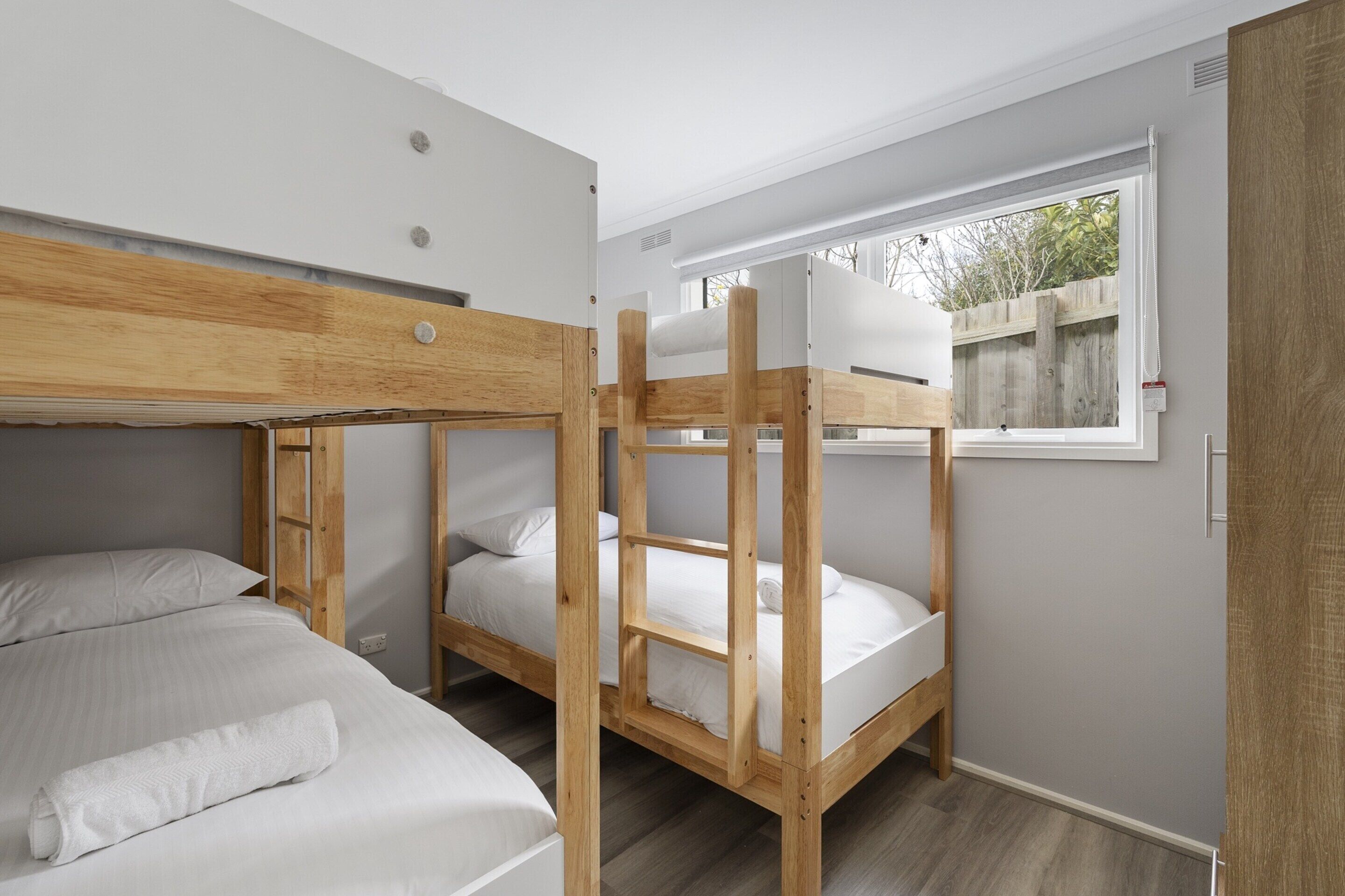 Ein Schlafraum mit Etagenbett, Fenster, Holz-Kopfteil und weißer Bettwäsche.