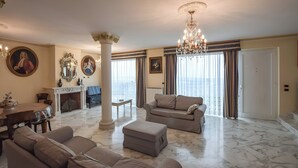 Uma sala de estar ampla com lareira, um candelabro e uma grande janela com cortinas.
