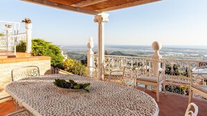 Uma área de estar coberta ao ar livre, com mesa e cadeiras, com vista para uma paisagem deslumbrante.