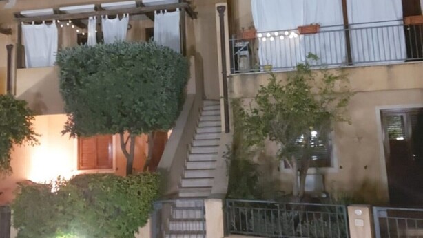 A multi-story building with a staircase leading to the upper floors, surrounded by greenery and a balcony with string lights.