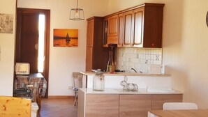 A kitchen with wooden cabinets, a tiled backsplash, a painting of a sunset, and a small dining area with a table and chairs.