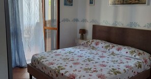 Une chambre à coucher comprenant un lit, une table de chevet, une lampe, une fenêtre avec des rideaux et un mur orné d’un motif décoratif.