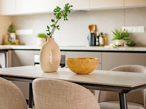 Eine moderne Küche mit einer weißen Arbeitsplatte, einer beige farbenen Vase mit Pflanze und einer Holzkugel.