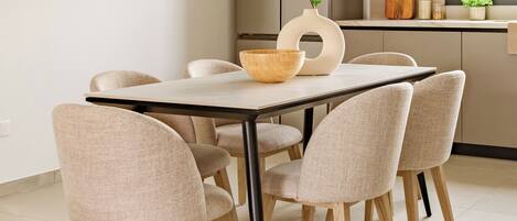 Un espace repas moderne avec une table en bois, six chaises rembourrées et un vase agrémenté de plantes vertes.