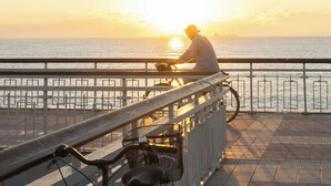 A person sitting on a bench by a waterfront, overlooking the sea during sunset. - One Bedroom Apartment With Balcony and Seaview (Pomorie)