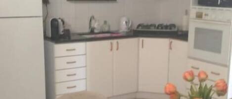 A compact kitchen with white cabinets, a black countertop, and a dining area with woven placemats.