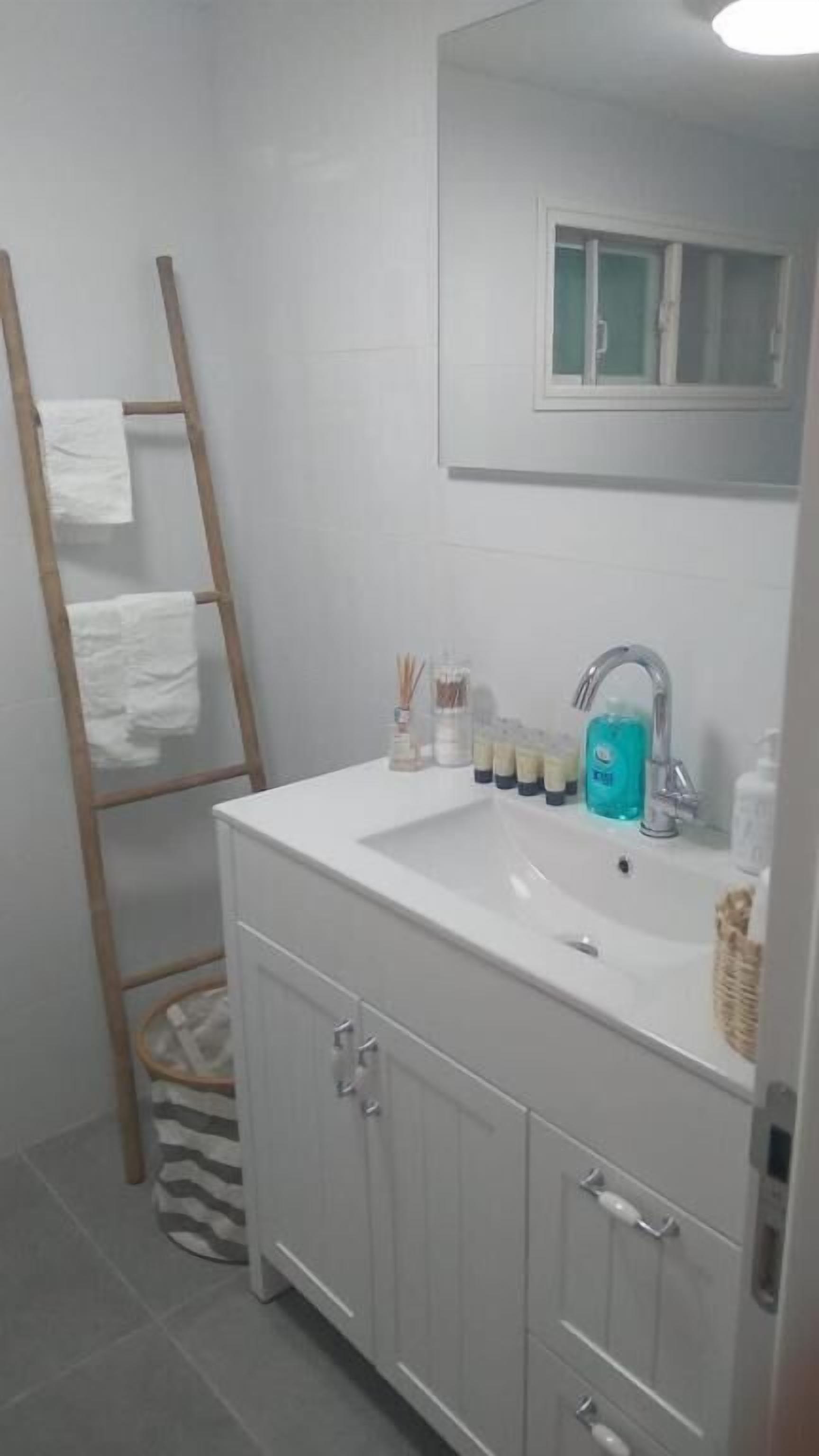 A bathroom with a white sink, a mirror above it, and a wooden ladder with white towels hanging on it.