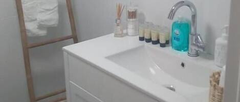 A bathroom with a white sink, a mirror above it, and a wooden ladder with white towels hanging on it.