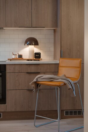A modern kitchen with wooden cabinets, a built-in stove, and a chair with a blanket. - Bright & Stylish Apartment (Tromsø)